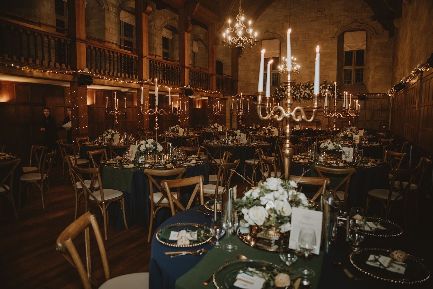 Elegant wedding reception in a historic hall with green tablecloths, tall candelabras, and floral centerpieces.