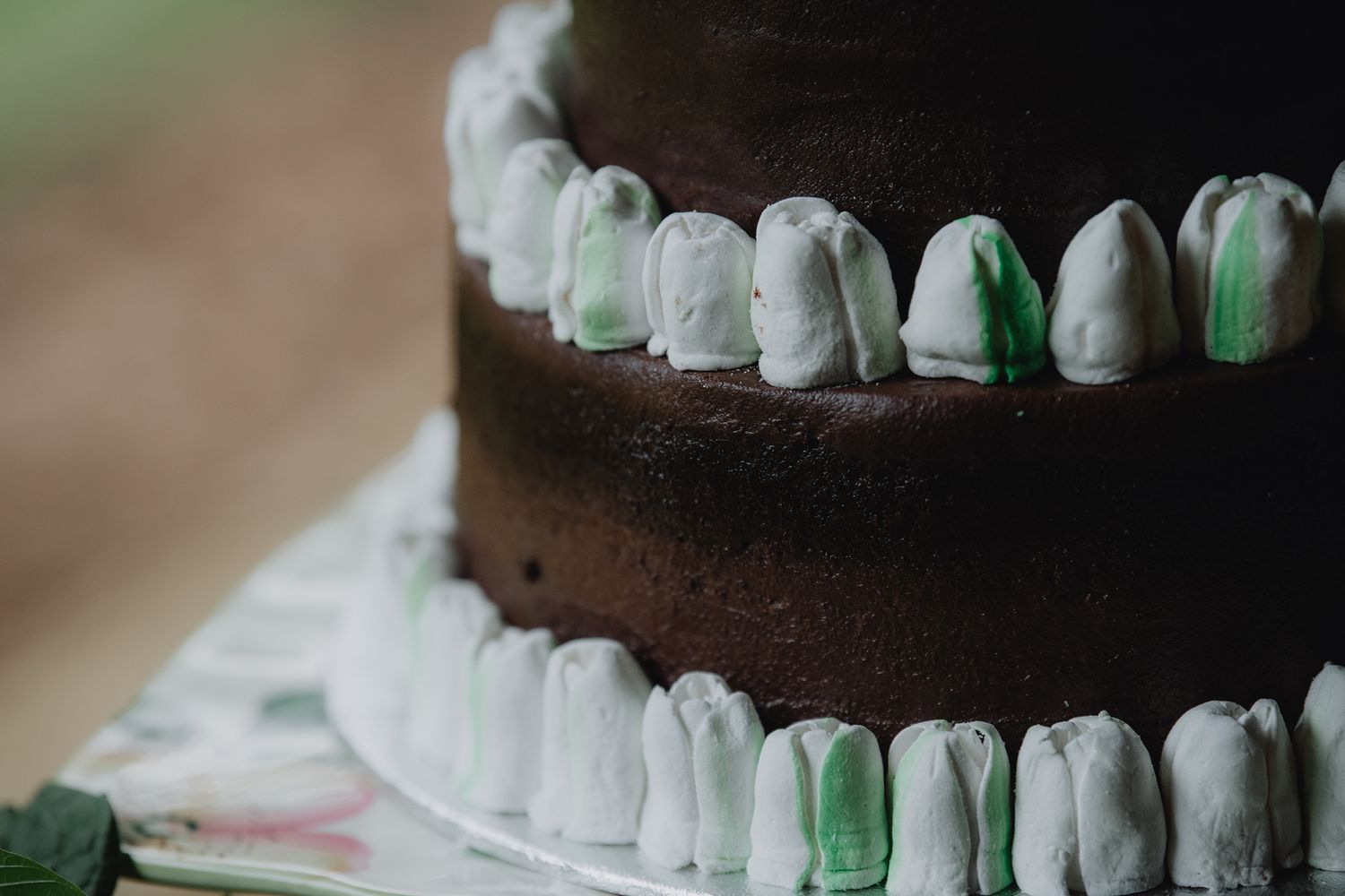 Close-up of chocolate wedding cake decorated with green and white buttercream tulip piping.