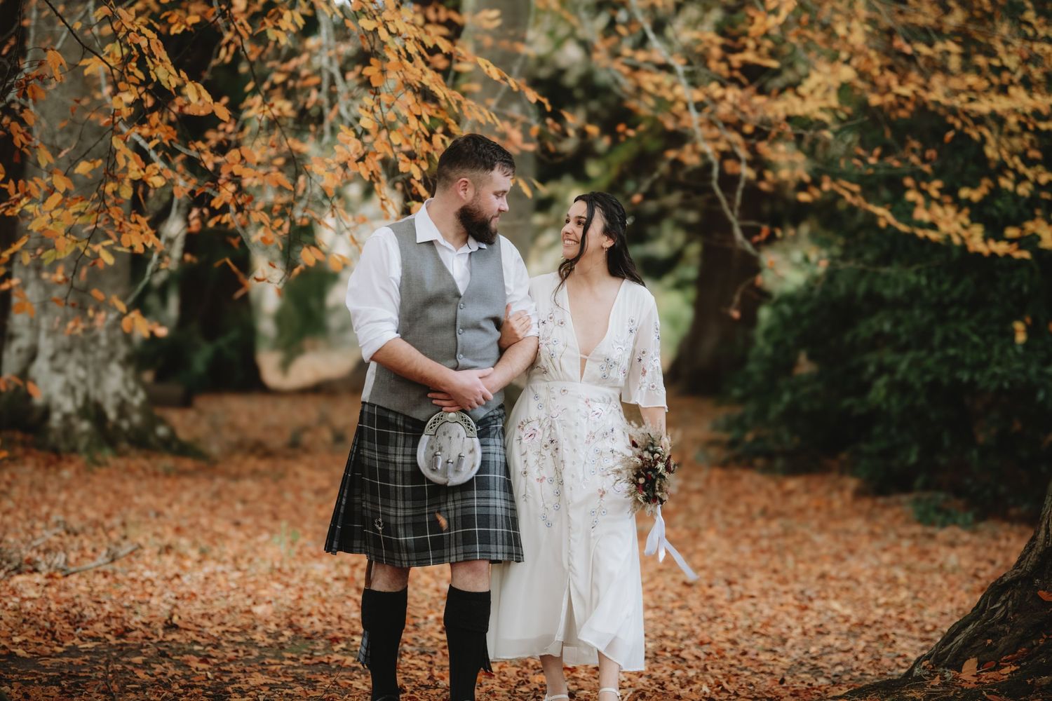 Bride and groom share romantic moment in autumn woodland, groom wearing traditional Scottish tartan kilt.