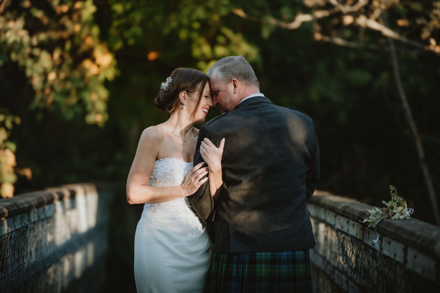 Bride and groom share an intimate forehead touch on a stone bridge surrounded by autumn trees.