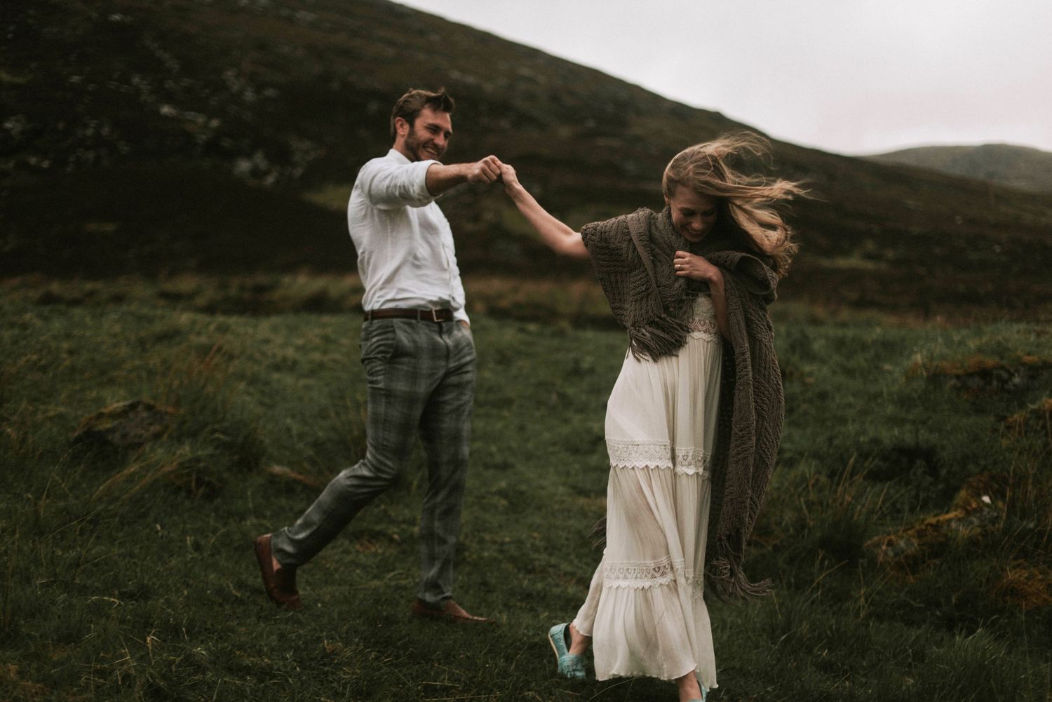 Couple dancing playfully in green Scottish Highland meadow on a windy overcast day.