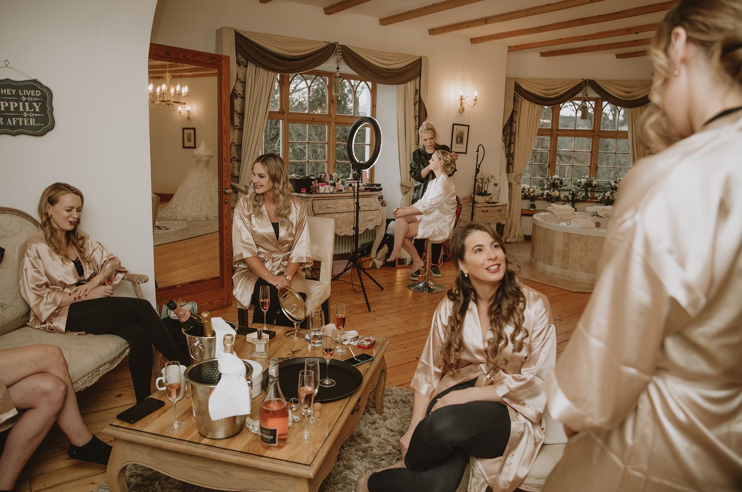 Bridesmaids in satin robes relaxing in elegant room with champagne during bridal party getting ready.