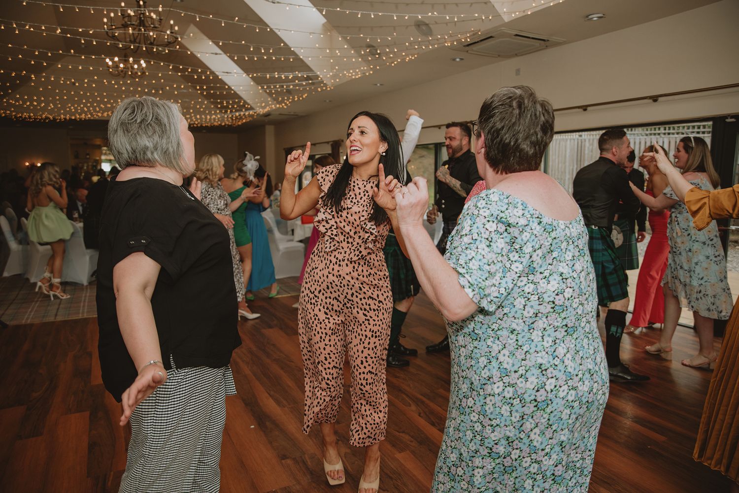Guests dancing joyfully at a wedding reception in an elegantly decorated venue with fairy lights.