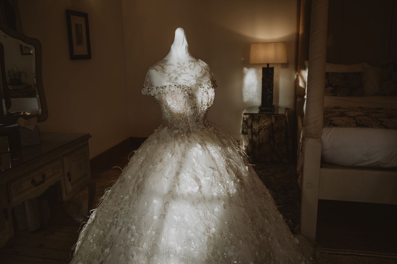 Elegant white ball gown wedding dress displayed in a dimly lit hotel room, featuring intricate lace detailing and full skirt.