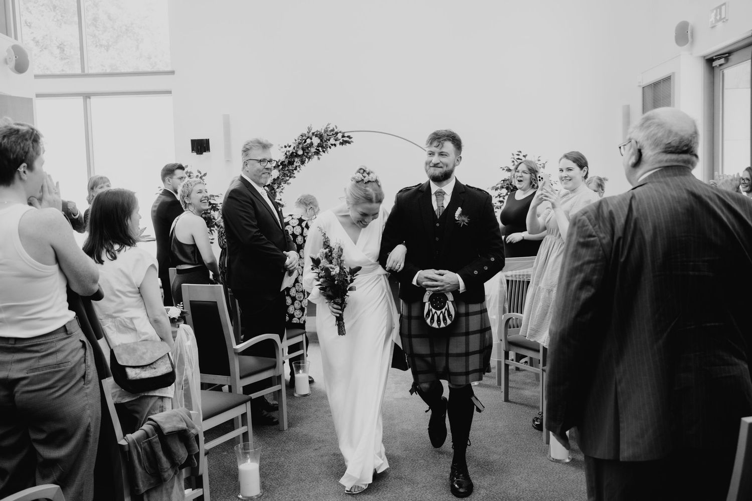 Bride and groom walk back down the aisle after wedding ceremony, groom wearing traditional Scottish kilt.