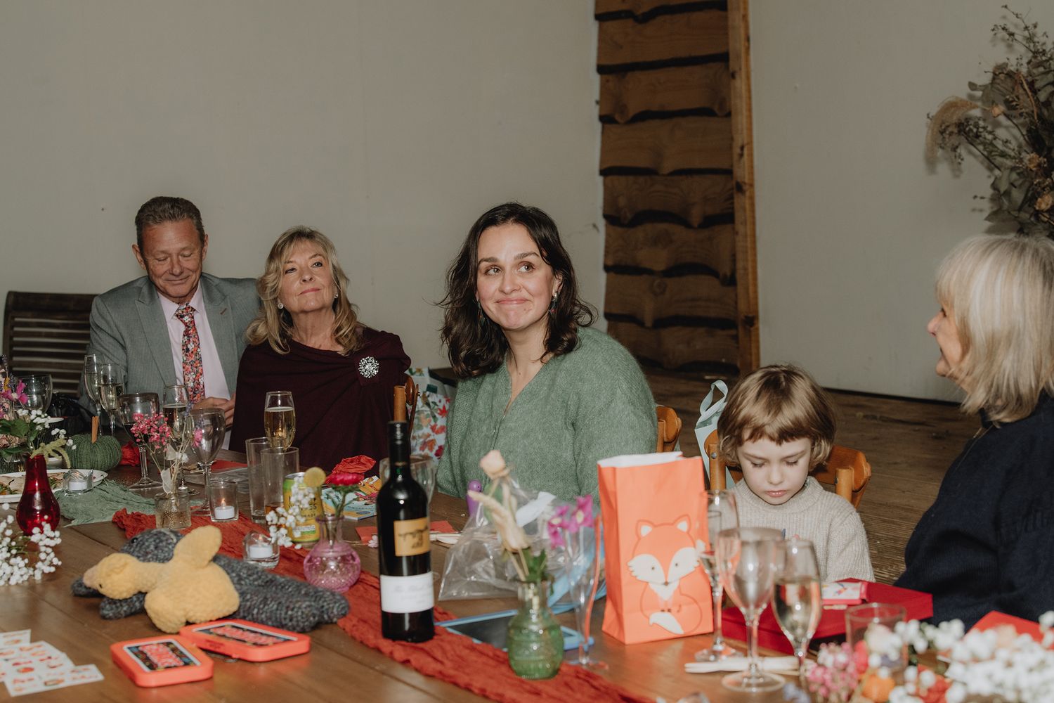 Family gathered around a festive holiday dinner table with wine, decorations, and colorful gifts in a cozy dining room.