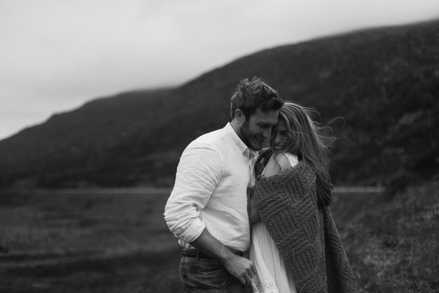 Black and white intimate portrait of couple embracing tenderly in misty Scottish Highland valley.