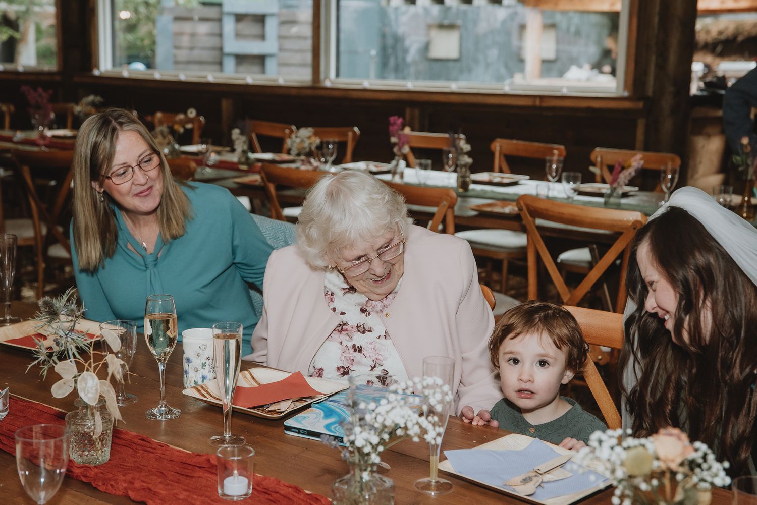 Three generations of women smile together at a decorated wedding reception table.