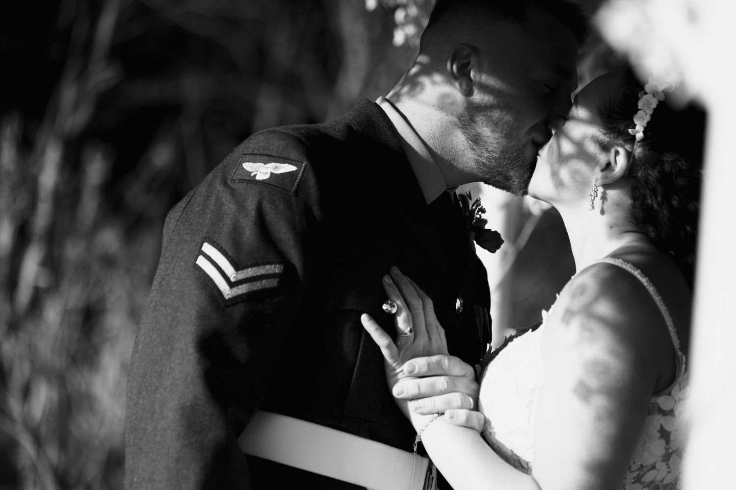 Intimate black and white portrait of bride and groom sharing tender kiss, groom in military dress uniform.