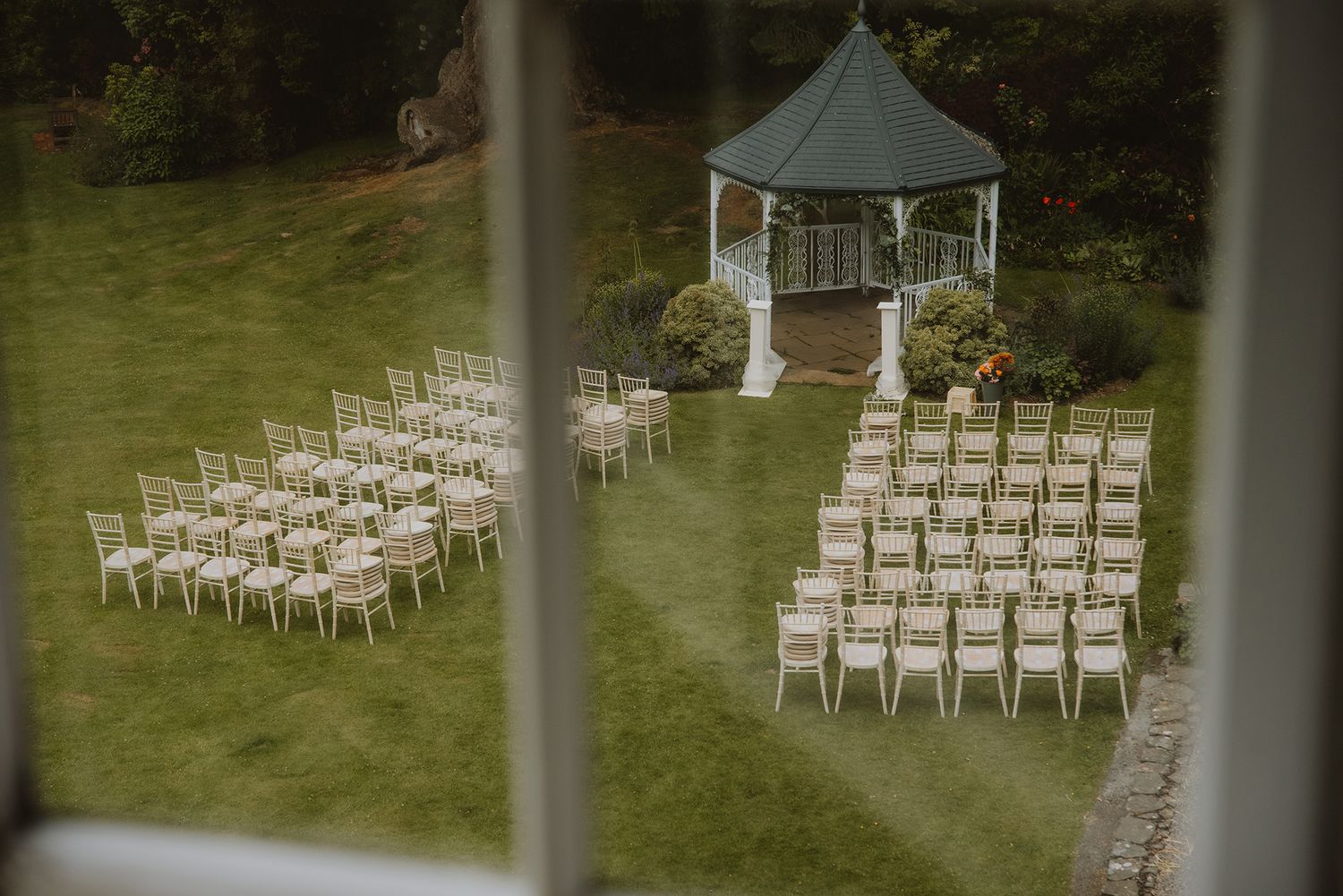Aerial view of outdoor wedding ceremony setup with white chairs and gazebo on green lawn.