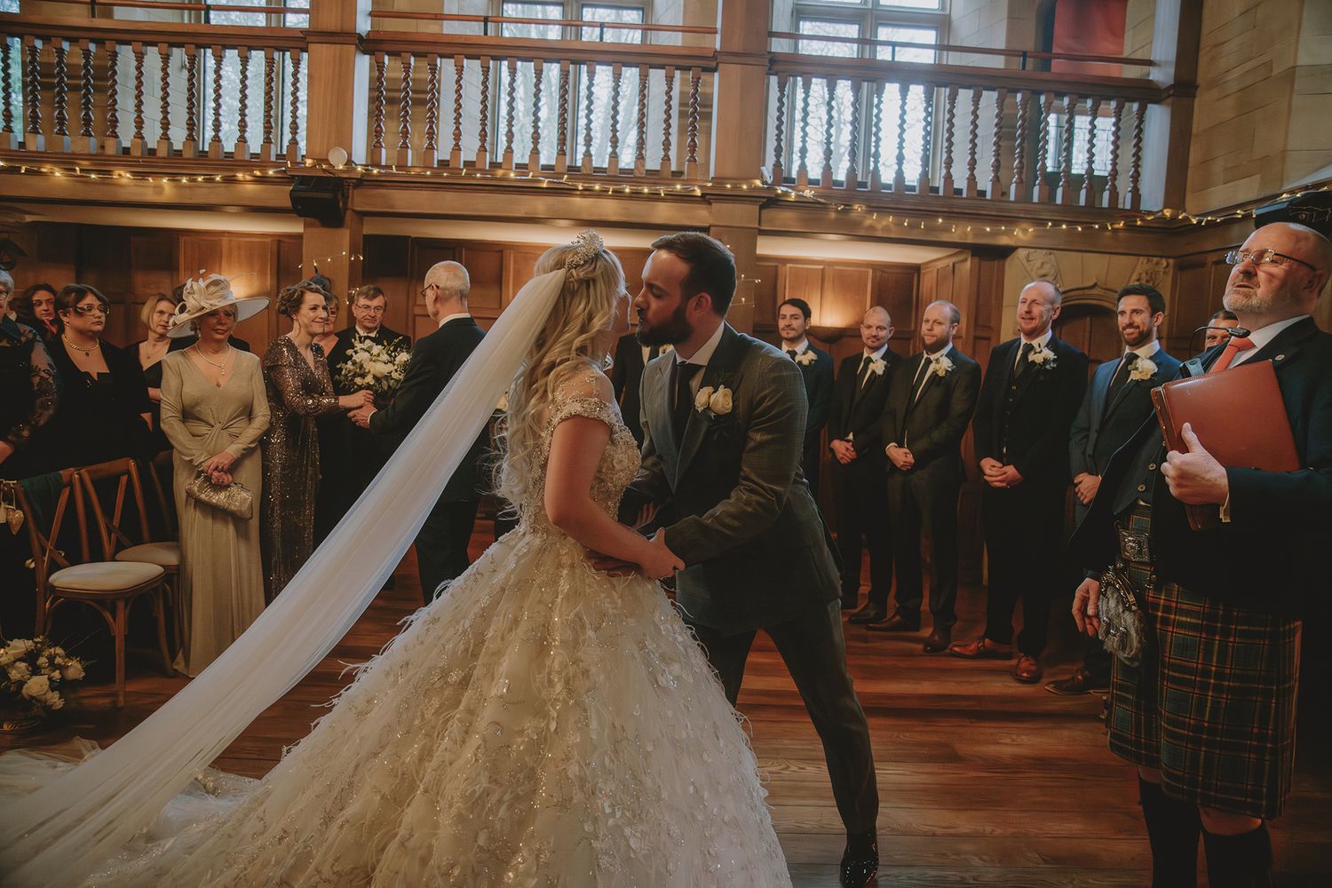 Bride and groom share first kiss at elegant Scottish castle wedding ceremony with guests watching.