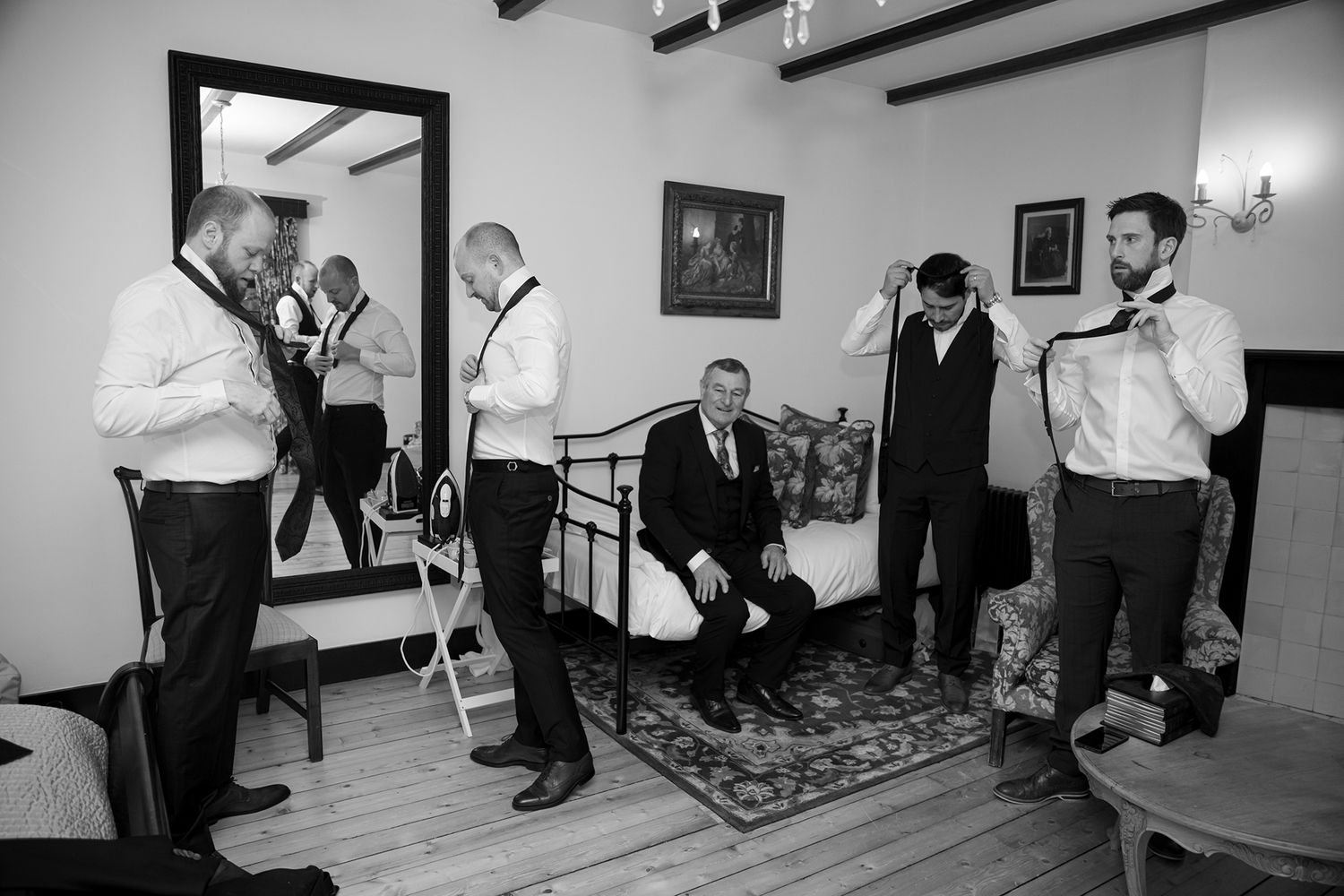 Groomsmen in white shirts and suspenders helping each other get ready in a classic room.