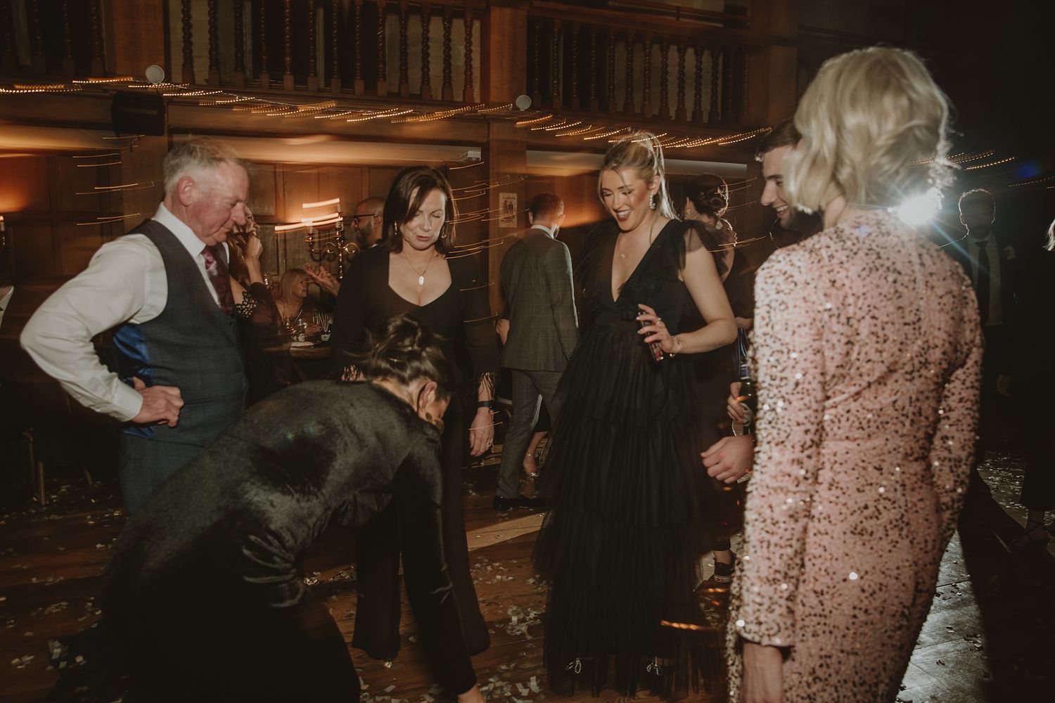 Elegantly dressed guests mingle at a glamorous evening event in a warmly lit venue with festive decor.