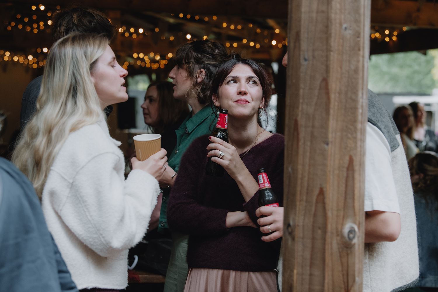 Two women socializing at an outdoor evening event with warm string lights.