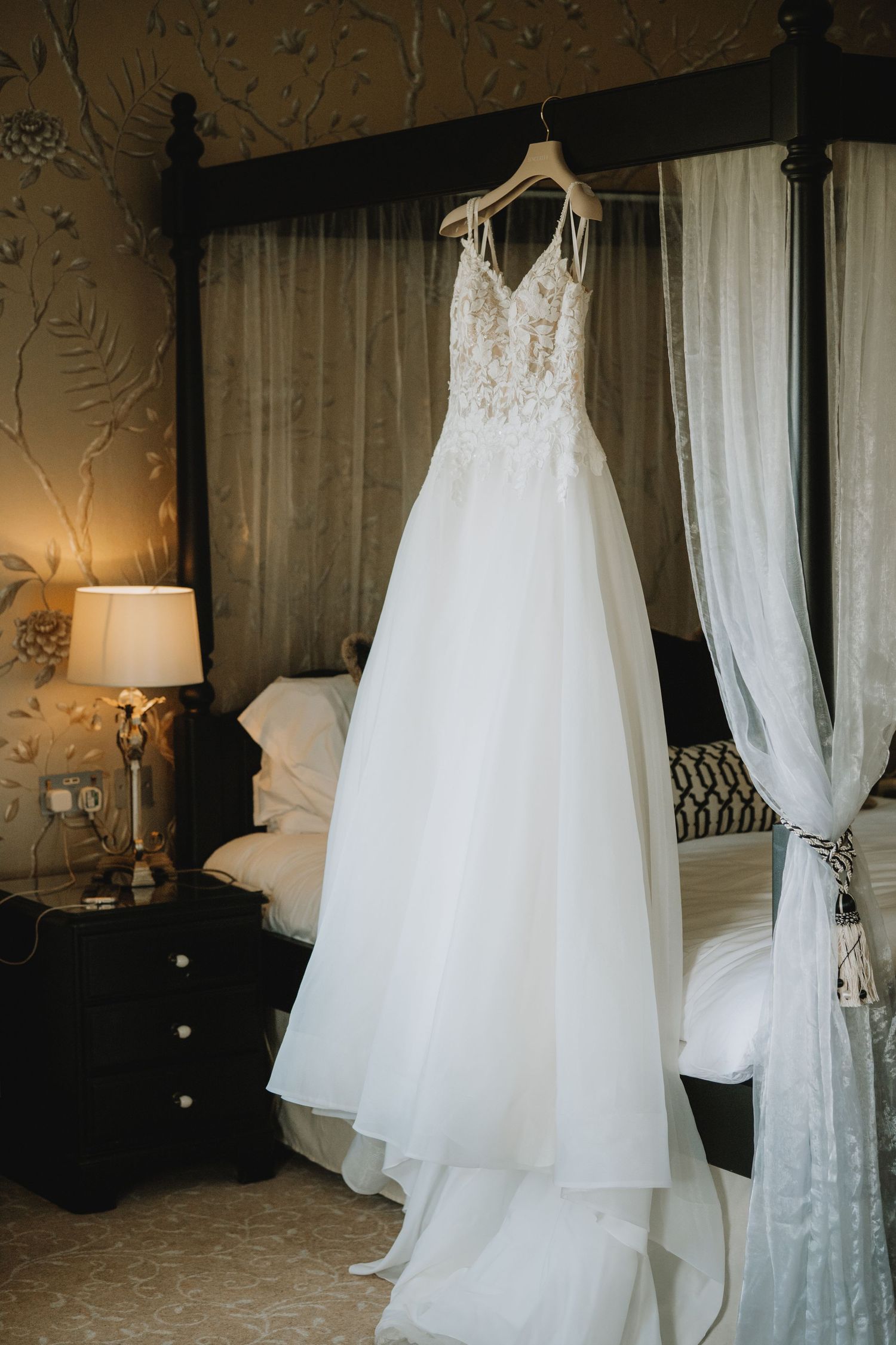 Elegant A-line wedding dress with lace bodice hanging from four-poster bed in luxurious bridal suite.