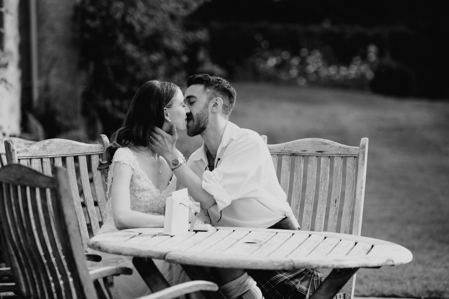 Black and white photo of bride and groom sharing a tender kiss at outdoor wooden table.