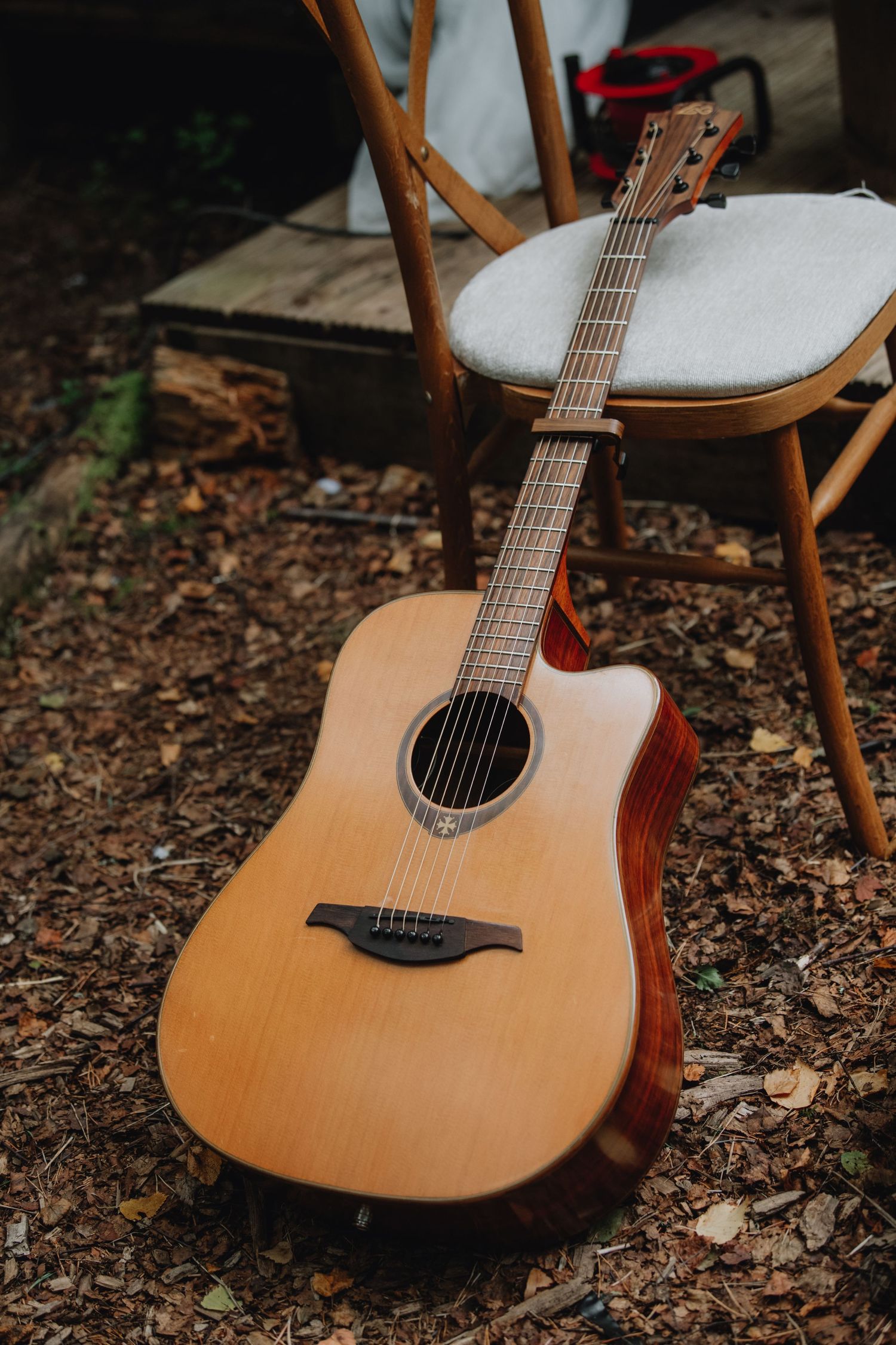 Acoustic cutaway guitar leaning against vintage wooden chair on mulch ground at outdoor wedding.