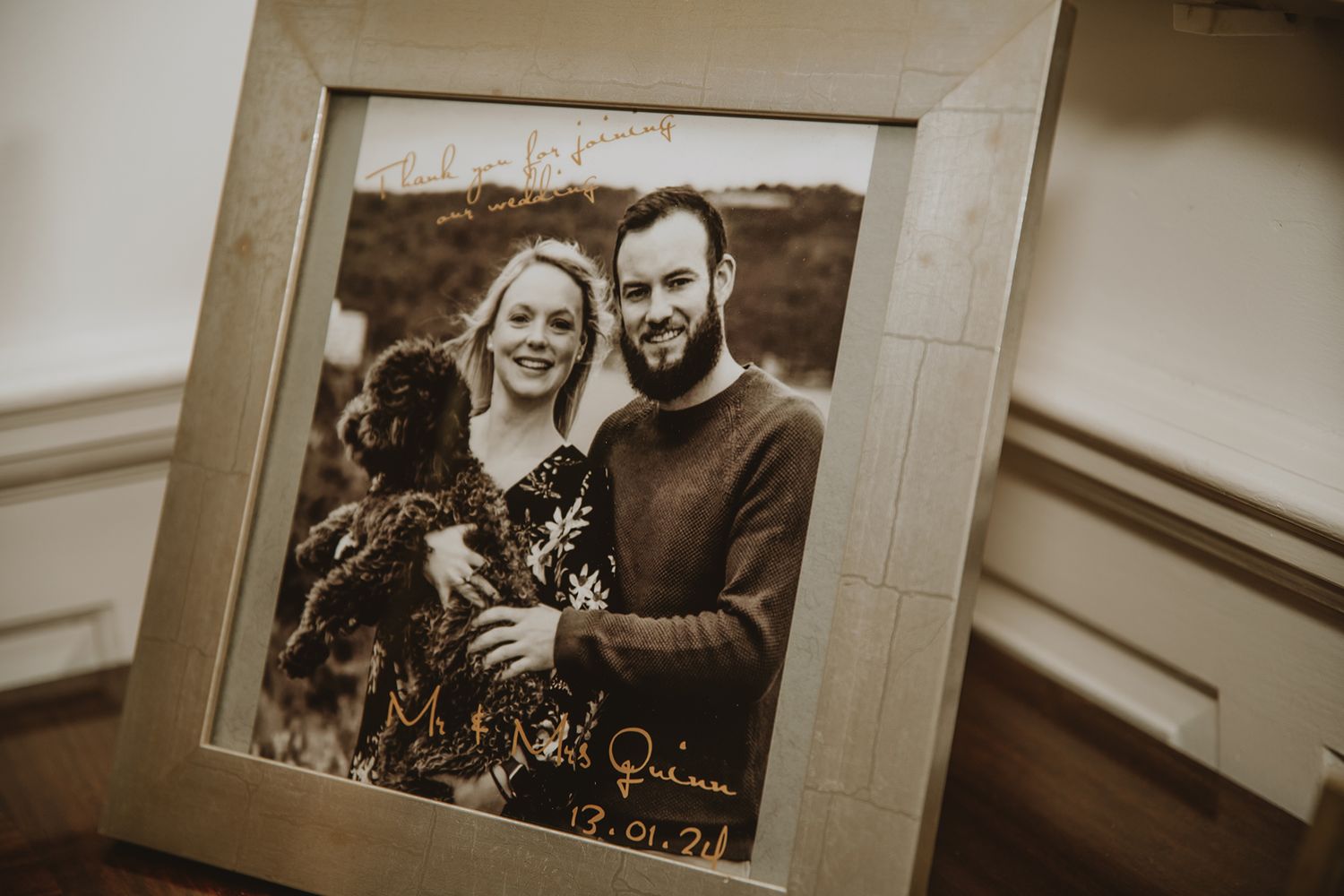 Framed engagement photo of smiling couple with dog, signed with names and date in elegant script.