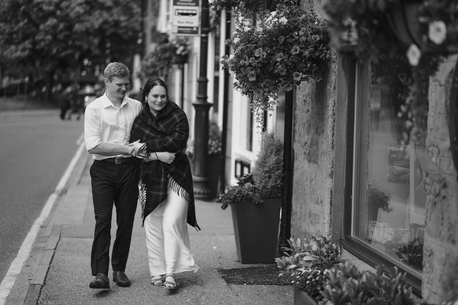 Couple walking together along a charming street lined with hanging flower baskets and storefronts.