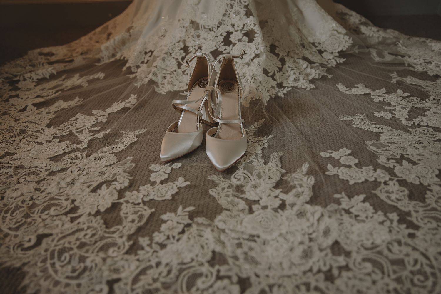 White lace wedding dress spread flat with elegant ivory heeled bridal shoes placed at center.