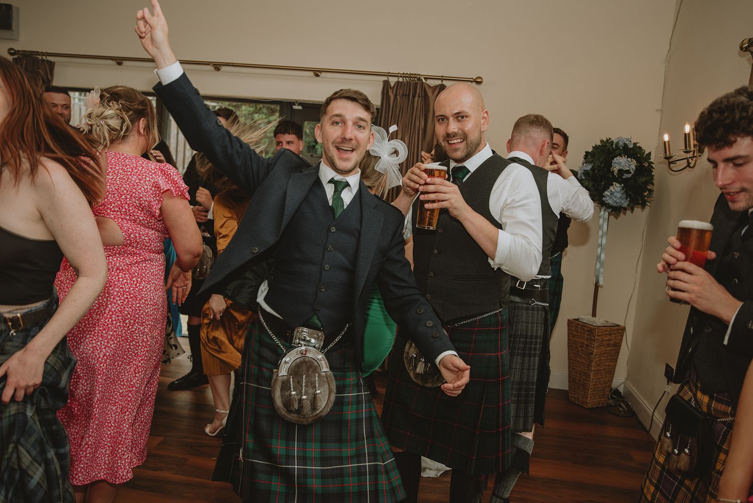 Men in traditional Scottish kilts celebrate joyfully at a lively wedding reception party.