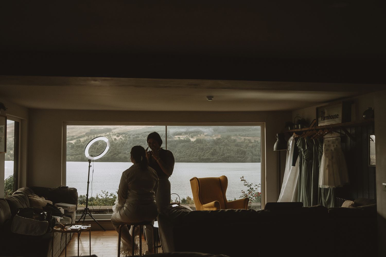 Silhouette of bride and groom looking out large window overlooking scenic lake in dimly lit room.