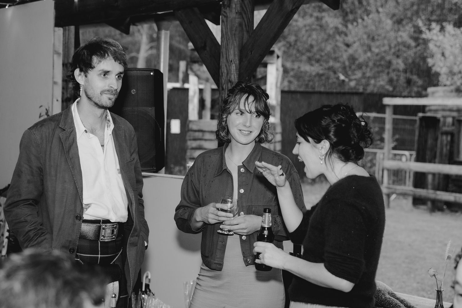 Three guests socializing outdoors at a casual wedding reception in black and white photo.