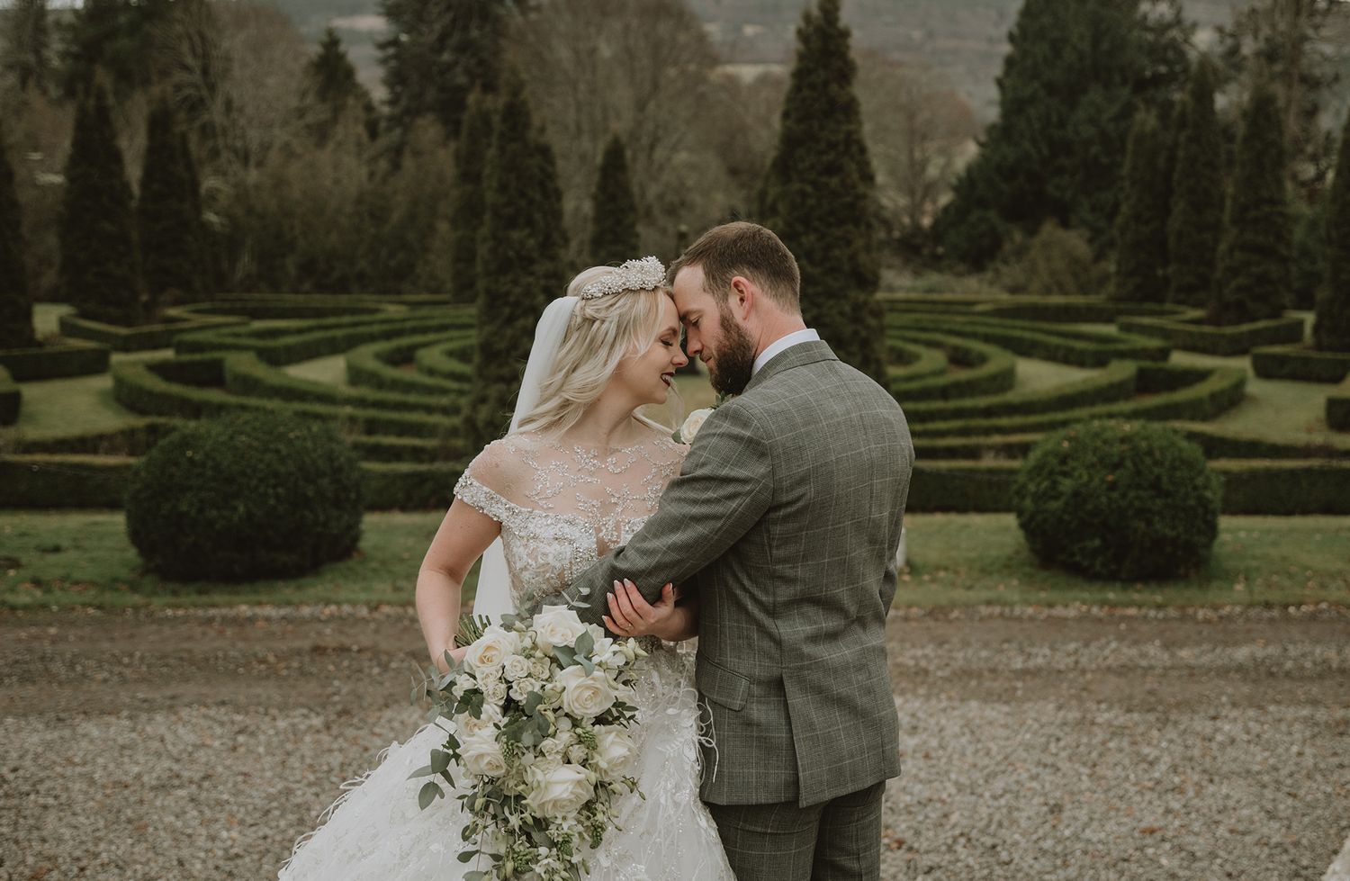 Bride and groom share a romantic moment in a formal garden with manicured hedges on their wedding day.