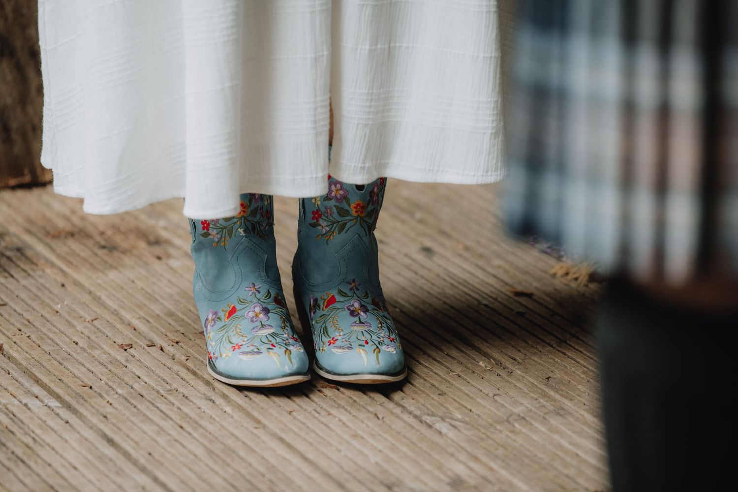 Bride wears decorative blue floral embroidered boots with white wedding dress at outdoor ceremony.