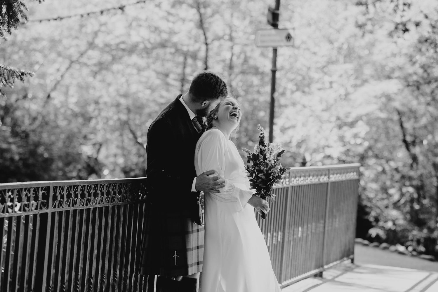 Black and white photo of bride and groom sharing a tender moment on a balcony surrounded by lush trees.
