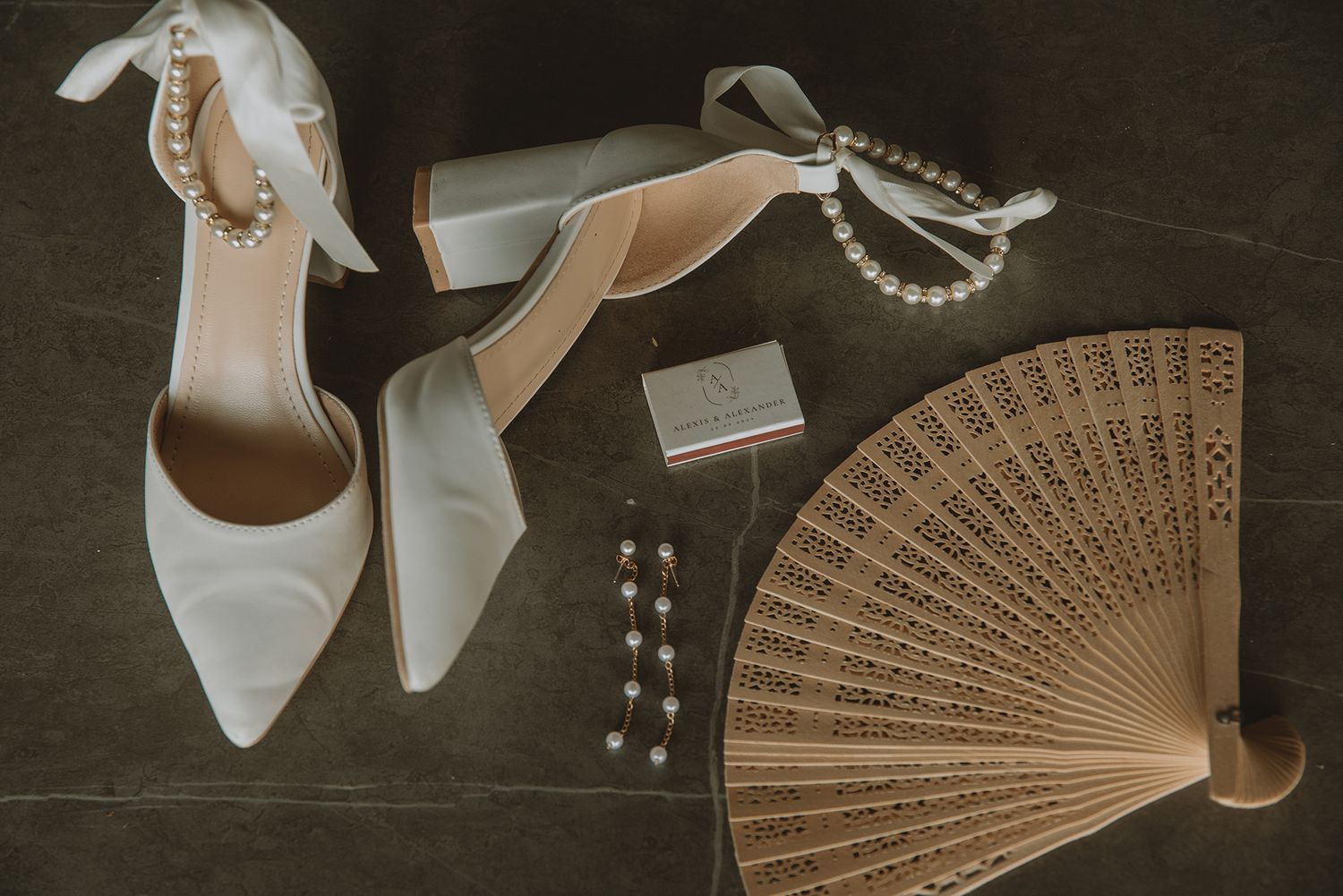 Elegant wedding accessories flat lay featuring white heels with pearl anklets, fan, and pearl jewelry.