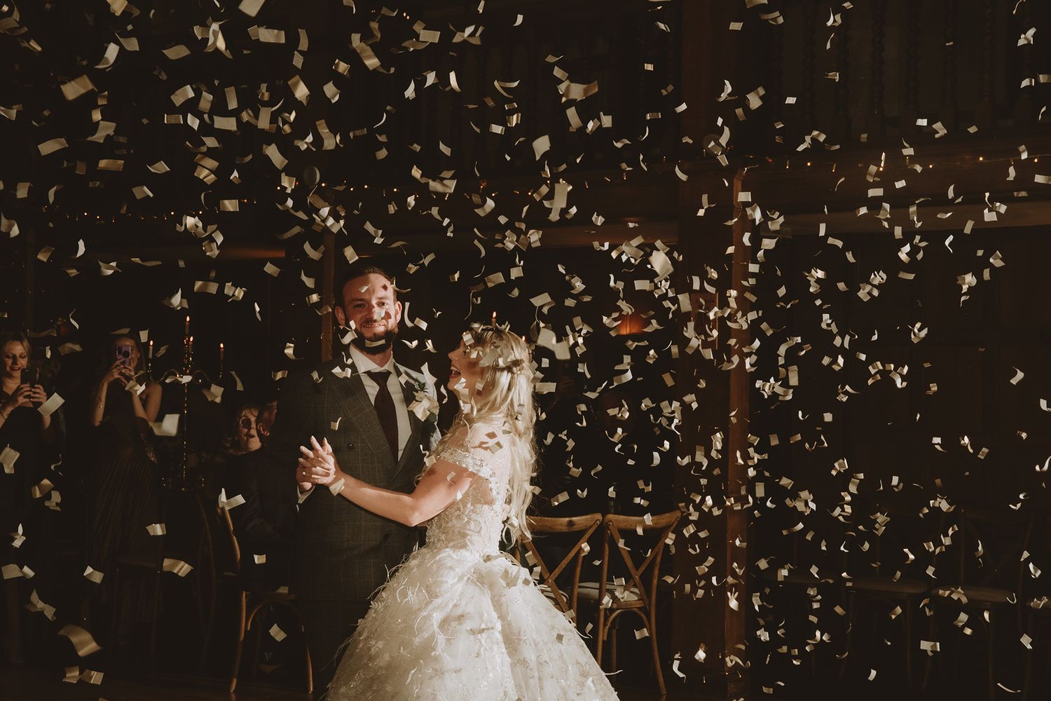 Bride and groom share first dance surrounded by falling gold confetti at elegant wedding reception.