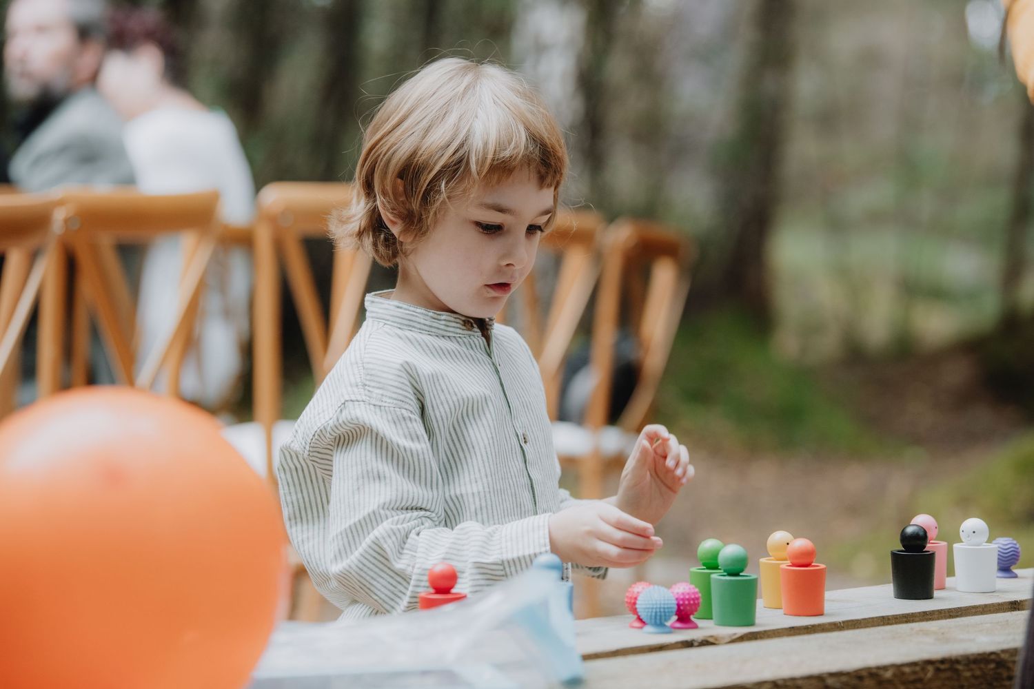 Young child with braided hair playing with colorful paint bottles at an outdoor wedding activity table.