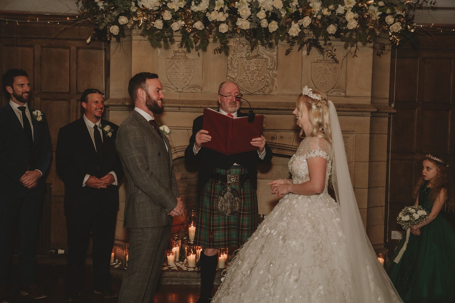 Couple exchange vows at candlelit Scottish castle wedding with officiant in traditional kilt attire.