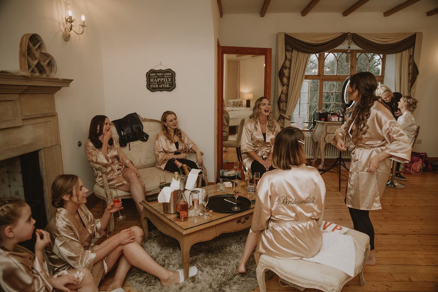 Bridesmaids in matching champagne satin robes gather in an elegant room, relaxing and celebrating before the wedding ceremony.