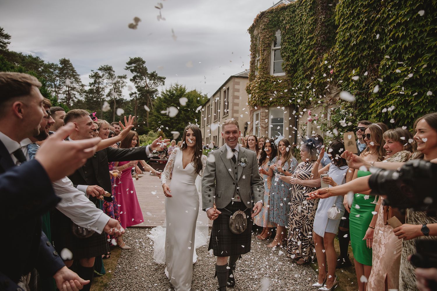Newlywed couple walking through confetti shower with wedding guests celebrating outside a historic venue.