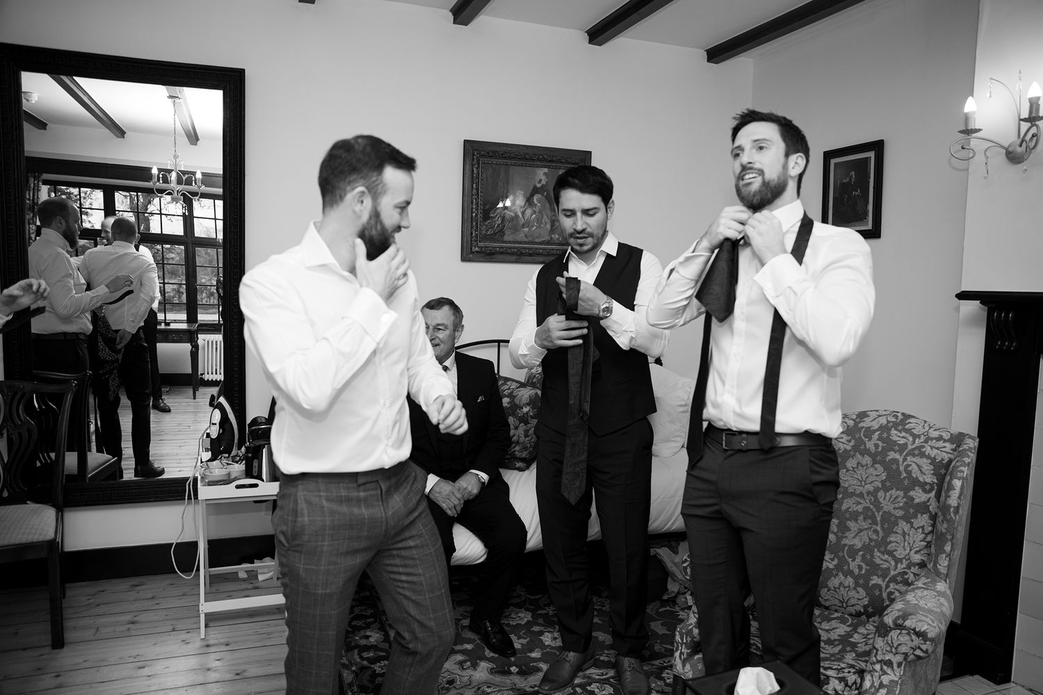 Groomsmen adjusting ties and suspenders in black and white wedding preparation photo.