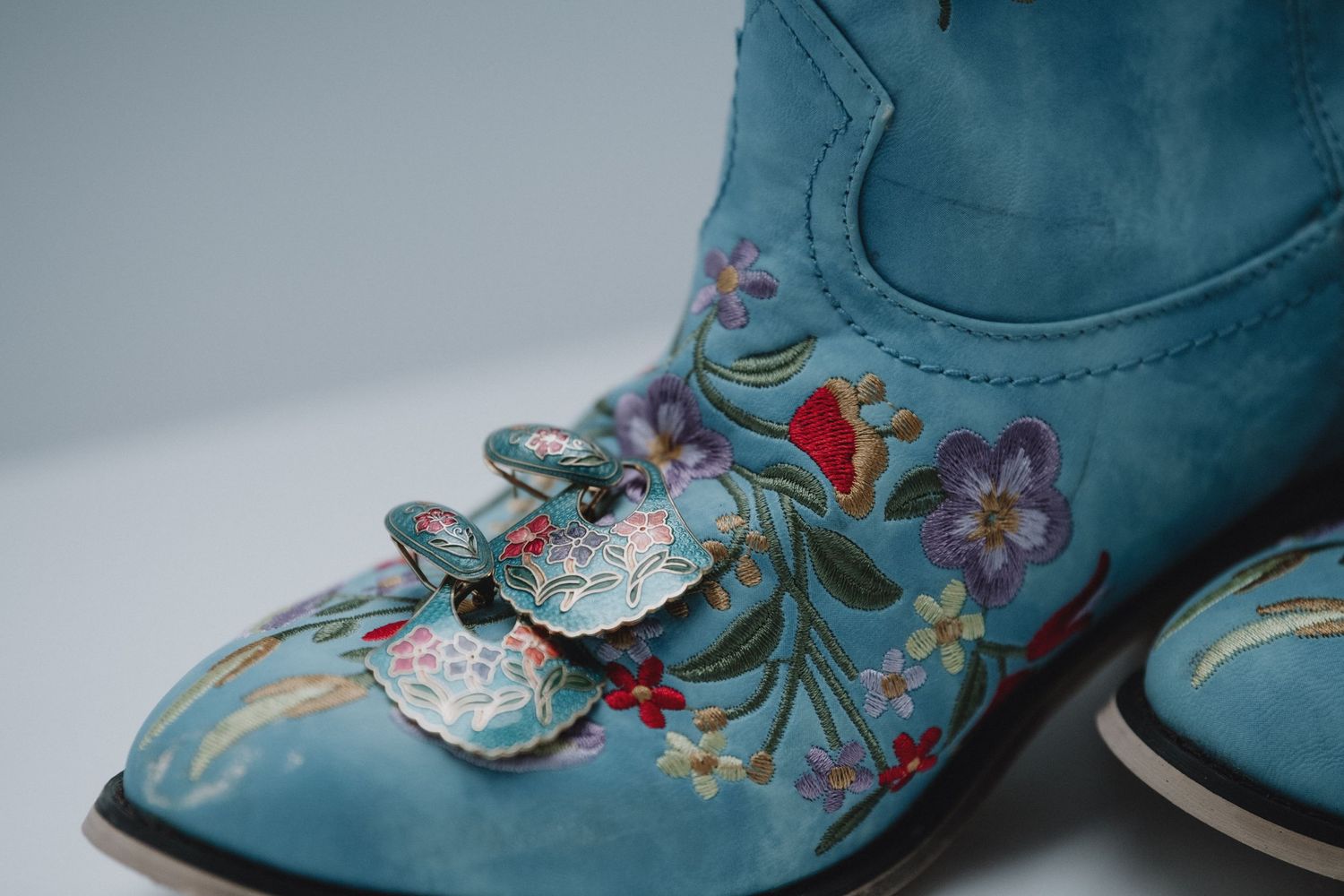 Close-up detail of turquoise cowboy boots with intricate floral embroidery and decorative charm.