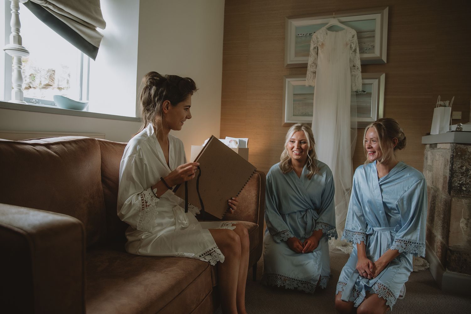 Bride and bridesmaids in robes share a joyful moment reviewing wedding photos on a sofa.