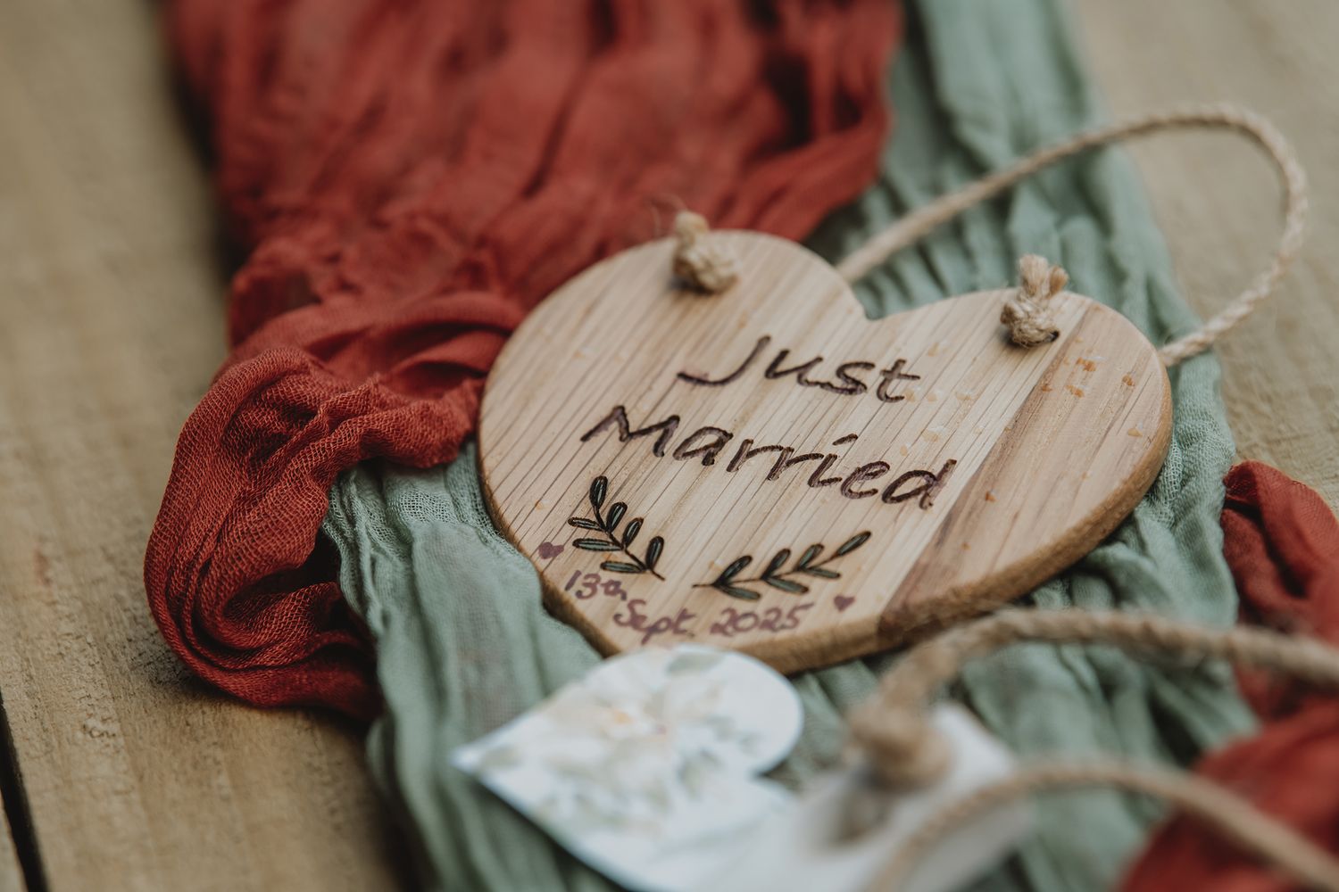 A wooden heart-shaped Just Married sign with floral engraving rests on colorful rustic fabric.