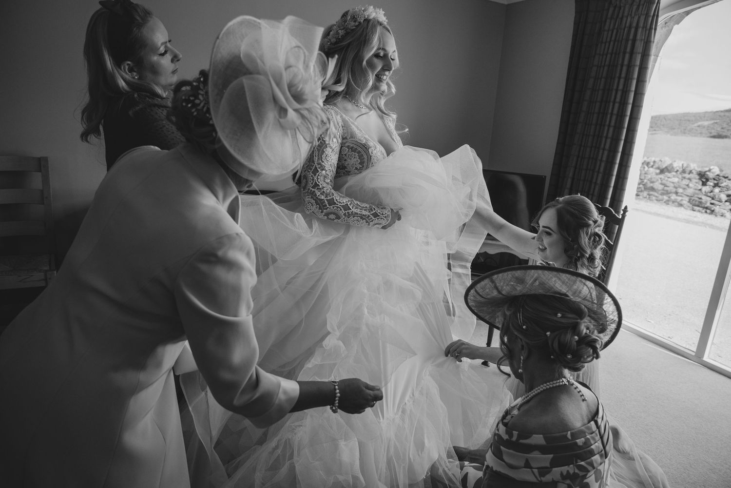 Bride being helped into wedding dress by family members in black and white photo.