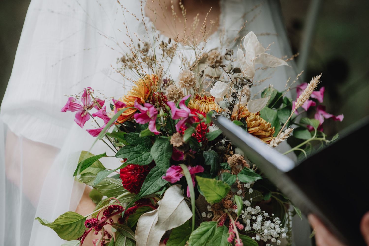 Close-up of vibrant wildflower bridal bouquet with pink, red and green blooms at woodland wedding.