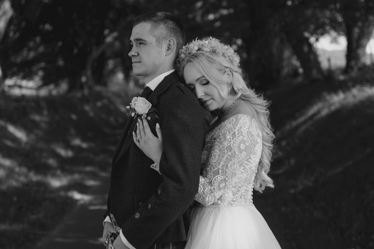 Bride leaning on groom in black and white intimate wedding portrait outdoors.