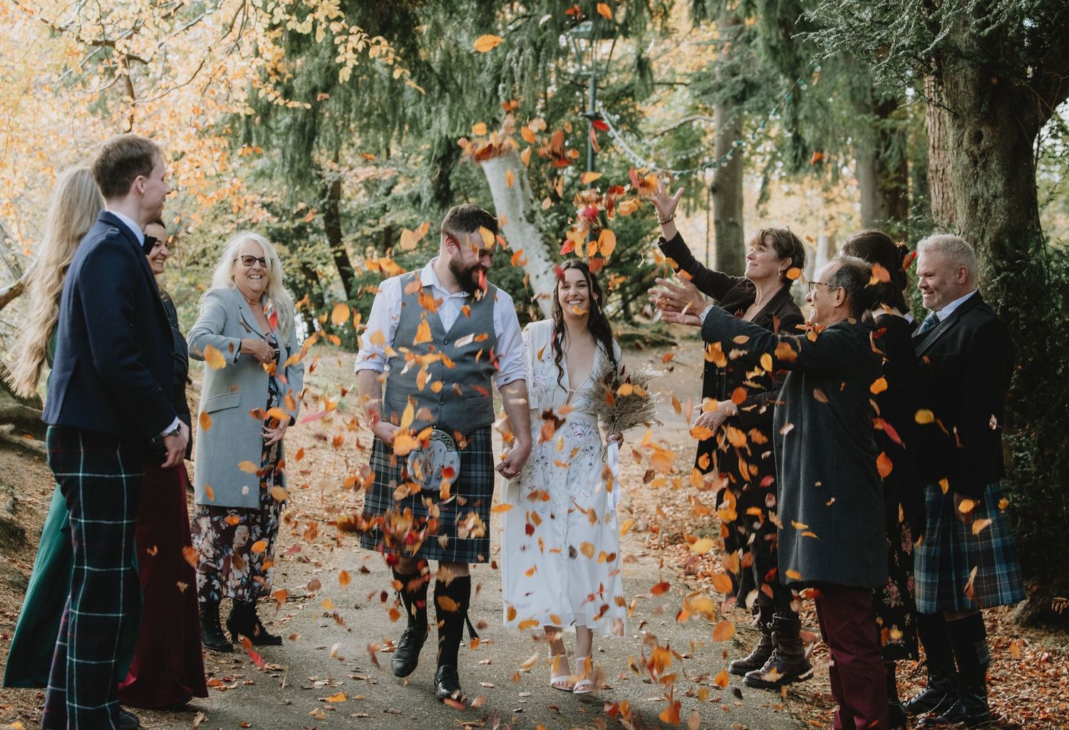 Autumn wedding confetti throw in woodland setting with guests tossing orange leaves over bride and groom.