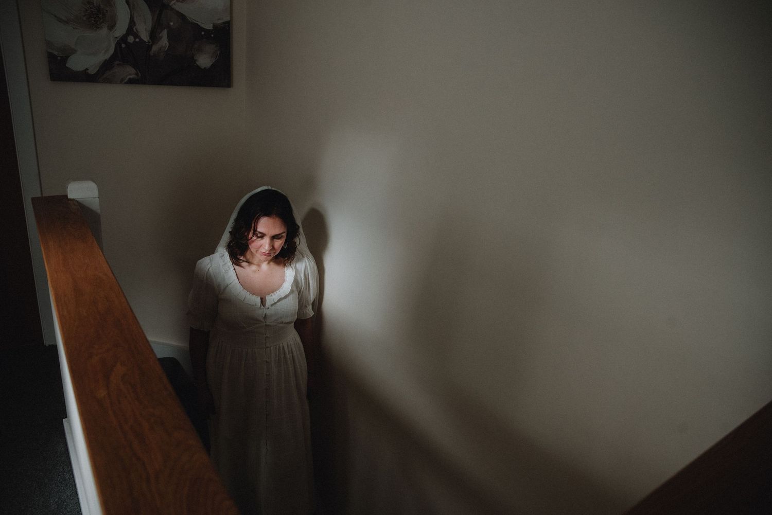 Bride in white wedding dress and veil ascending staircase in dramatic moody lighting before ceremony.