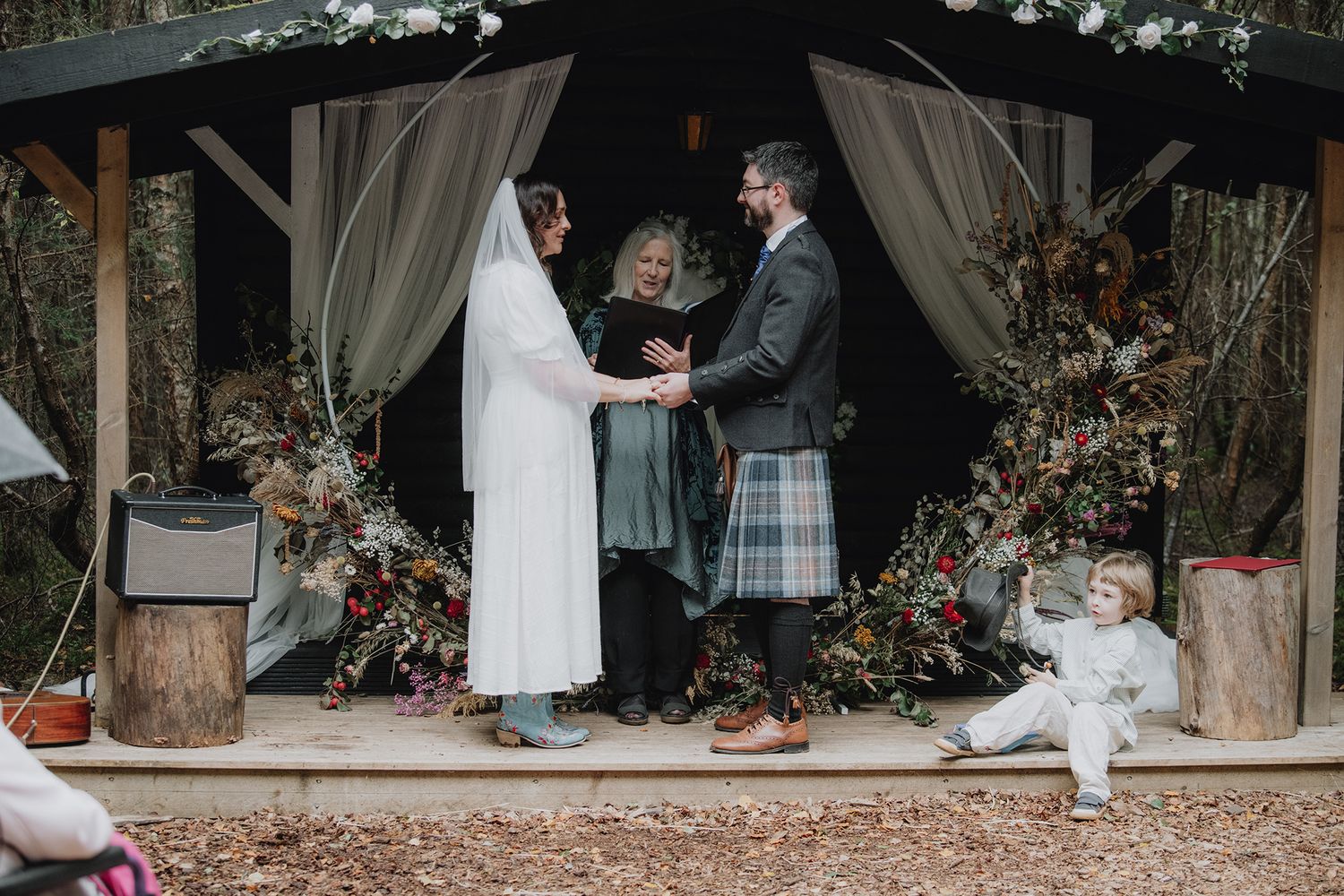 Couple exchange vows in rustic outdoor woodland ceremony decorated with dried floral arrangements.