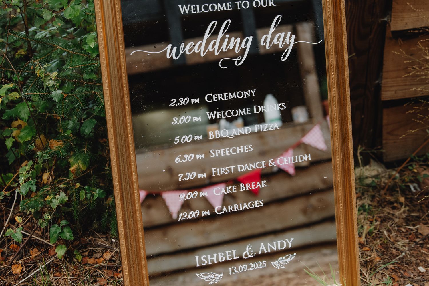 An elegant gold-framed wedding day schedule mirror sign for Ishbel and Andy dated 13.09.2025.