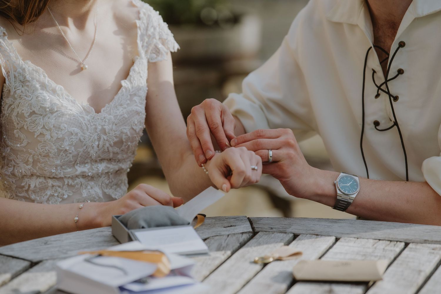 Close-up of bride and groom exchanging rings at rustic wooden table during intimate wedding ceremony.