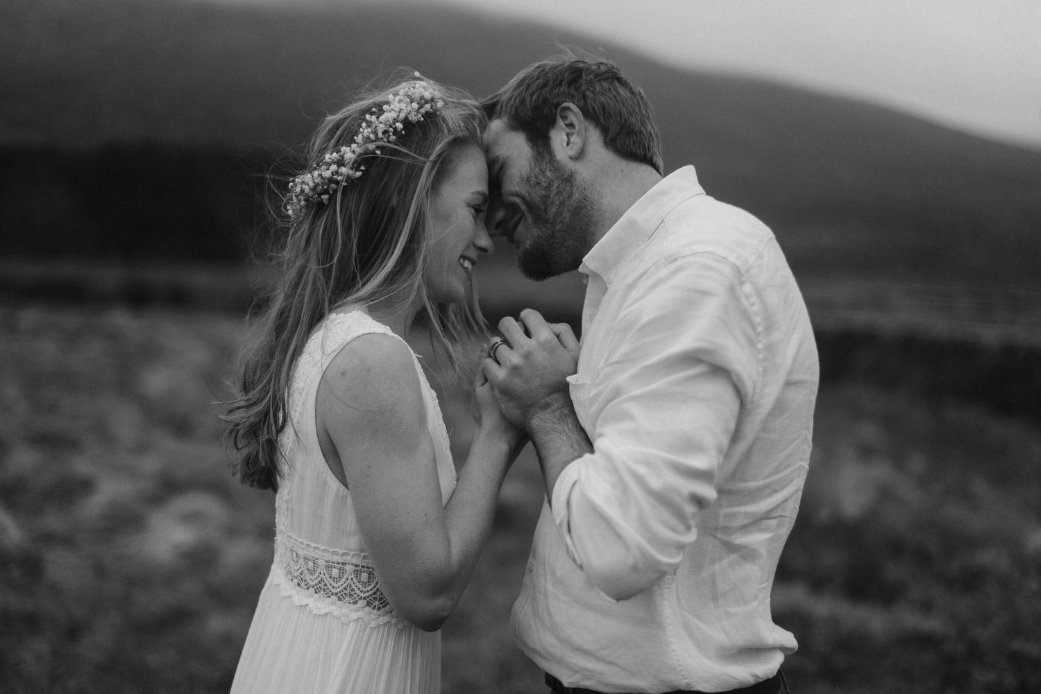 Black and white photo of a romantic couple holding hands and smiling in an open field.
