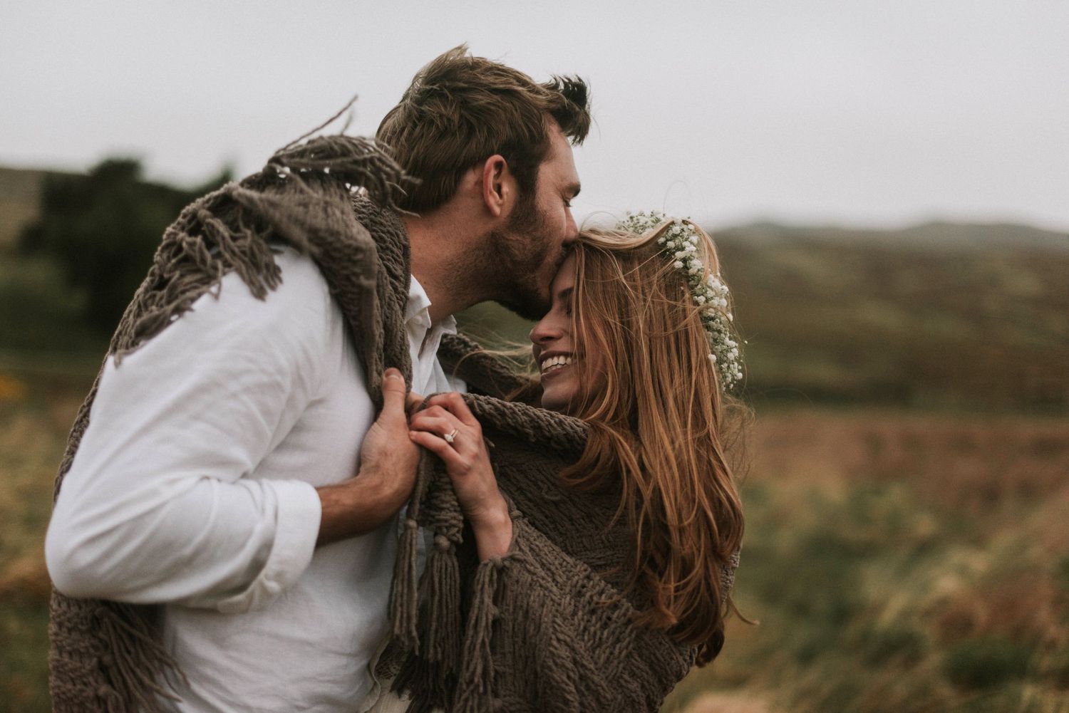 Couple sharing a romantic kiss wrapped in a blanket with bride wearing a flower crown.